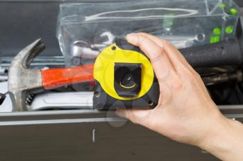 Horizontal photo of female hand taking used tape measure out of toolbox 