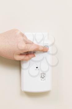 Vertical photo of carbon monoxide alarm with female hand testing the system