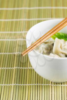 Close up vertical photo of freshly made wonton with chopsticks on top of white bowl 