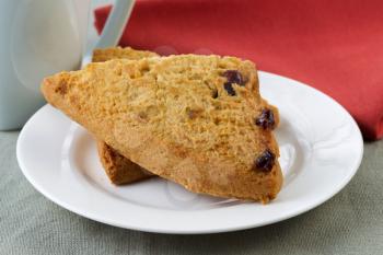 Closeup horizontal photo of scones on white plate with tea cup plus red napkin in background