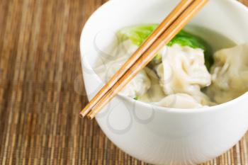 Extreme close up horizontal photo of freshly made wonton with chopsticks on top of white bowl 