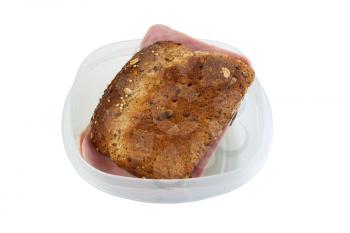 Horizontal photo of a ham sandwich made with whole grain bread inside of plastic container isolated on white