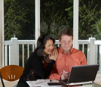 Photo of close mature couple working at home with laptop, calculator and papers on top of table and large windows in background