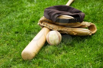 Horizontal photo of old baseball, bat, cap and glove on natural grass field 