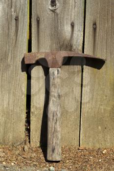 Vertical photo of an old hammer lying against aged fence 