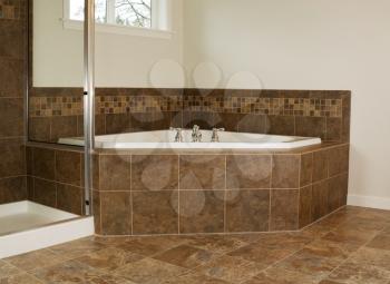Horizontal photo of soaking tub in master bathroom with partial shower and windows 