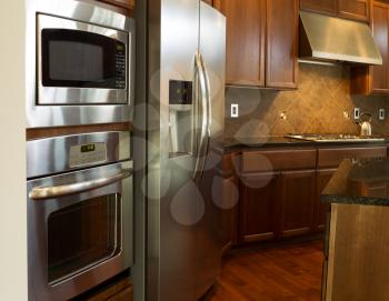 Closeup photo of a stainless steel appliances in modern residential kitchen with stone counter tops and cherry wood cabinets with hardwood floors 