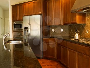 Closeup photo of a walkway behind Kitchen Island with stainless steel appliances, gas stove, stone counter tops and cherry wood cabinets with hardwood floors 