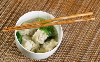 Close up horizontal top view photo of freshly made wonton with chopsticks on top of white bowl 