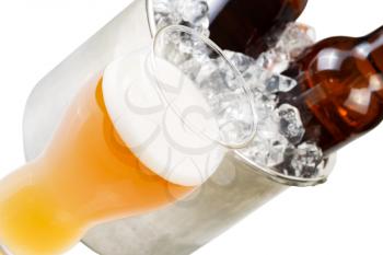 Closeup angled horizontal photo of freshly poured beer in large glass and bottled beer in stainless steel bucket filled with ice isolated on white