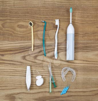 Overhead view of dental maintenance tools placed on aged wooden boards. Items include hand tooth brush, picks, whitening trays, gel, mirror, floss, toothpaste tube, and electric tooth brush. 