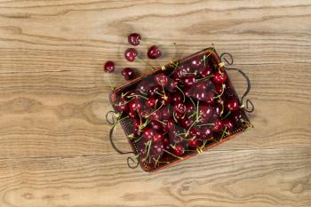 Horizontal overhead view of fresh black cherries in basket onto rustic wooded boards