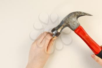 Horizontal photo of female hands holding hammer and nail on interior home white wall