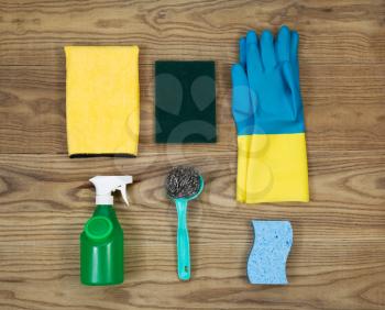 Overhead view of house cleaning materials placed on rustic wood.  Items include sponge, rubber gloves, stainless steel pad, spray bottle, microfiber rag, and scrub pad. 