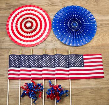 Overhead view of six United States of America flags, ribbons and large pinwheels positioned on rustic wooden boards.  