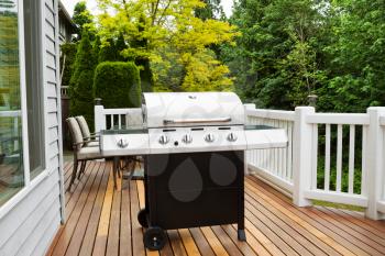 Closeup horizontal photo of BBQ grill on open cedar patio with seasonal trees in full bloom in background 