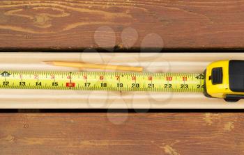 Horizontal photo of tape measure and pencil on top of new cedar wood board next to fading wood on outdoor wooden deck 