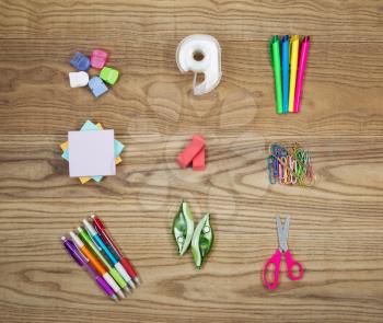Overhead view of office supplies placed on rustic wood.  Items include hanging clips, tape, high light markers, note paper, erasers, paper clips, pens, correction ink, and small scissors.  
