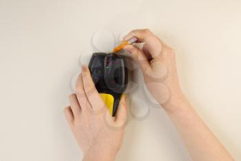 Photo of female hands holding using stud finder and pencil against interior home white wall