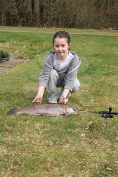 Vertical photo of young girl proudly displaying her large fish while kneeling on the ground