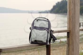 Horizontal photo of a hiking backpack on wooden fence with ocean in background