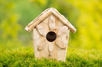 Horizontal view of new wooden birdhouse outdoors with blurred out bright yellow and green leaf trees in background during summer day