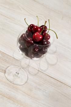 Angled vertical image of fresh black cherries in glass on aged wood