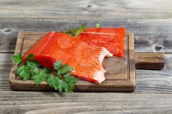Horizontal photo of fresh raw red salmon fillet on traditional wooden server with parsley on the side and rustic wood underneath 
