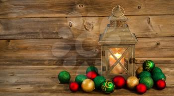 Horizontal front view of an old Asian design lantern and white candle glowing brightly inside with Christmas Ornaments on rustic wood