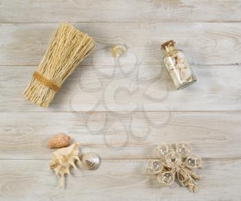 Overhead view of house decorations placed on rustic wooden boards. Items include seashells, shells in bottle, glass ornaments, and a bundle of tied straw

