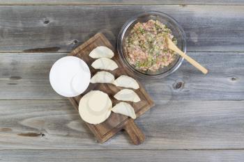 Overhead view of raw ingredients used to make Chinese Dumplings. Items consist of raw pork, green onions, wrappers, spoon, bowl of water, and wooden server