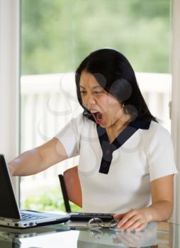 Vertical image of mature woman angrily glaring at her computer screen while working from home with blurred out daylight coming in from window in background