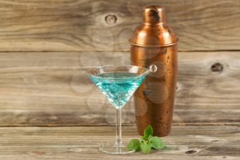 Horizontal photo of a mixed drink, fresh mint leaves, stir stick and a metal mixer resting on rustic wood
