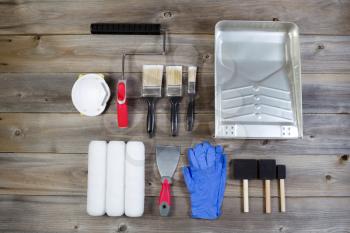 Overhead view of new painting accessories on rustic wood consisting of paint brushes, roller covers, pan, applicators, mask, latex gloves, scraper and hand roller frame