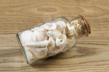 Horizontal view of a glass bottle filled with sea shells on rustic wood