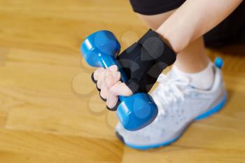 Horizontal image of female hand wearing workout glove while lifting small dumbbell weight with wooden gym floor in background  