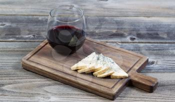 Horizontal photo of sliced blue cheese on a traditional walnut wooden server with a glass of red wine all underneath rustic wooden boards 