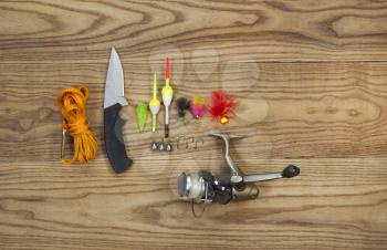 Horizontal top view photo of fishing lures, bobbers, sinkers, hooks, knife, reel and stringer on faded wood
