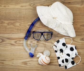 Overhead view of beach attire placed on rustic wooden boards.  Items include snorkel, mask, bikini, sea shells, and white hat. 