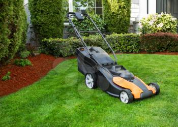 Photo of electric lawnmower on freshly cut plush green grass with home and flower beds in background 