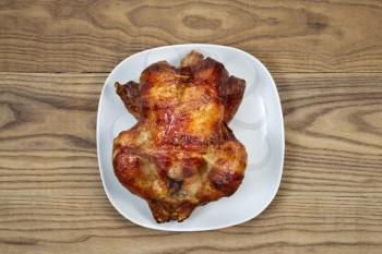 Overhead view of a freshly oven roasted whole chicken in white serving plate placed on rustic wood