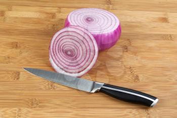 Closeup horizontal photo of freshly sliced red onion with kitchen knife in front and natural bamboo wood underneath