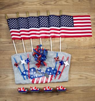Overhead view of United States of America flags, ribbons, t-shirt, fire cracker, dog tag and pinwheels positioned on rustic wooden boards.  