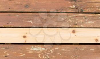 Horizontal photo of a single new cedar wooden board next to fading wood on outdoor deck 