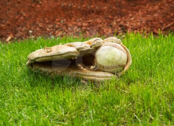 Closeup horizontal photo of old baseball inside of used glove on natural grass field 