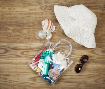 Overhead view of outdoor kit placed on rustic wooden boards.  Items include clear plastic bag, comb, sun screen, hair clips, sea shells, sun glasses and white hat. 