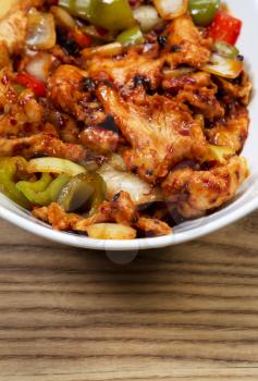 Closeup vertical view of Chinese spicy chicken dish in white bowl with rustic wooden boards underneath 