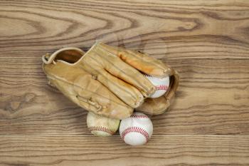 Horizontal top view photo of old baseball glove and balls on top of faded wood
