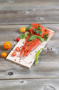 Vertical view of raw red salmon, skin side down, on maple wood grilling plank with seasoning and other herbs 