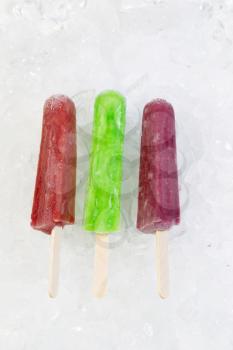 Vertical view of colorful frozen fruit popsicles on shaved ice